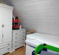 Innenraum eines Einfamilienhauses mit Bett, weißem Schrank und Boden in Holzoptik.