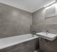 Badezimmer in einer 2-Zimmer-Wohnung mit Badewanne, Waschbecken und grauen Fliesen.