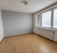 Ein leerer Raum in einer 3-Zimmer-Wohnung mit Holzboden und Fenstern mit Jalousien.