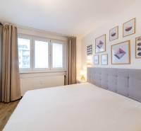 Helles Schlafzimmer mit Holzdekorboden, Bett und Wandbildern in einer Zweizimmerwohnung.