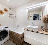 Badezimmer in einer 2-Zimmer-Wohnung mit Waschmaschine und Badewanne, helle Fliesen und Dekorationen.