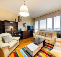 Wohnzimmer in einer 3-Zimmer-Wohnung mit Sofas, einem bunten Teppich und einem Holzboden.