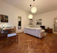 Wohnzimmer in einer Zweizimmerwohnung mit Holzboden, weißem Sofa und Tisch.