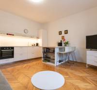 Wohnzimmer in einer 2-Zimmer-Wohnung mit Küche, Holzboden, Fernseher und Tisch.