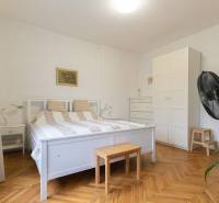 Schlafzimmer in einer Zweizimmerwohnung mit weißen Möbeln und einem Boden in Holzoptik.