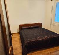 Schlafzimmer in einer 3-Zimmer-Wohnung mit Holzboden und dunkler Bettüberdecke.