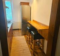 Eine schmale Küche in einer 3-Zimmer-Wohnung mit einem Gasherd, einem Kühlschrank und einem Holzboden.