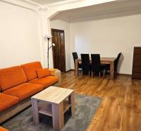 3-Zimmer-Wohnung mit einem orangefarbenen Sofa, einem Holztisch und einem Boden mit Holzdekor.