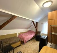 Ein Dachzimmer in einem Einfamilienhaus mit einfacher Möblierung und Dachbalken.