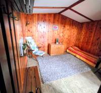 Ein Zimmer in einer Hütte mit Holzverkleidung, ein Sessel, eine Bank, ein Teppich und ein Bett.