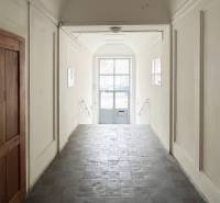 Ein Flur mit Fliesen und weißen Wänden führt zu einer verglasten Tür zur Vajnorská-Straße.