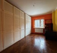 Ein Zimmer mit einer orangefarbenen Wand, einem großen Schrank und einem Boden mit Holzdekor in einer 3-Zimmer-Wohnung.