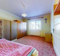 Schlafzimmer mit Bett, Schränken, Fenster und Kreuz in einem Einfamilienhaus.
