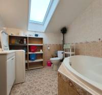 Badezimmer in einem Einfamilienhaus mit Badewanne, Waschmaschine, Regal und Dachfenster.