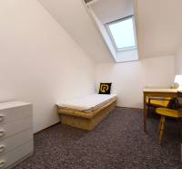 Einfaches Zimmer mit einem Bett, einem Tisch und einer Kommode in einem Einfamilienhaus.