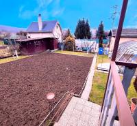 Ein gepflegter Garten bei einer Hütte in Partizánske, mit Hochbeeten und Bäumen rundherum.