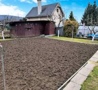 Garten mit Hütte in Partizánske, vorbereitetes Beet, umliegendes Grün und Holzhaus.