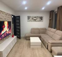 Wohnzimmer einer 3-Zimmer-Wohnung mit beigem Sofa, Fernseher und Boden in Holzoptik.