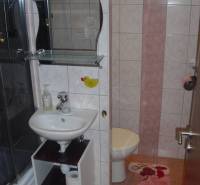 Badezimmer in einer Einzimmerwohnung mit Waschbecken, Duschkabine und hellen Fliesen.