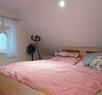 Ein Schlafzimmer im Dachgeschoss eines Einfamilienhauses mit Bett, Fernseher und einem Boden in Holzoptik.