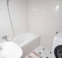 Badezimmer mit Duschwanne, Waschbecken und Waschmaschine in einer 4-Zimmer-Wohnung.