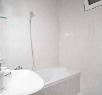 Badezimmer mit Badewanne und Waschmaschine in einer 4-Zimmer-Wohnung. Wände mit hellen Fliesen bedeckt.