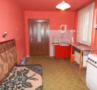 Eine Küche in einem Einfamilienhaus mit roten Wänden, älteren Möbeln und einem grünen Teppich.