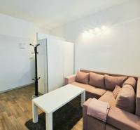 Einzimmerwohnung mit Ecksofa, weißem Tisch und Boden in Holzoptik.