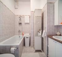 Badezimmer in einer Einzimmerwohnung mit Badewanne, Waschbecken und Keramikfliesen in neutralen Farbtönen.