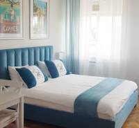 Schlafzimmer in einer Einzimmerwohnung mit blauem Bett, Kronleuchter und Holzboden.