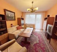 Wohnzimmer in einer 2-Zimmer-Wohnung mit älteren Möbeln, Teppich und dekorativen Vorhängen.