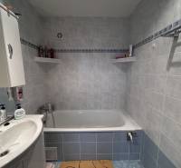 Badezimmer mit Badewanne, Waschbecken und Regalen in einer Zweizimmerwohnung mit blauen Fliesen.