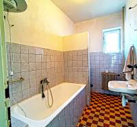 Ein Badezimmer in einem Einfamilienhaus mit einer Badewanne, einem Waschbecken, einem Heizkörper und Fliesen im Schachbrettmuster.