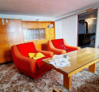 Ein Wohnzimmer in einem Einfamilienhaus mit älteren Sesseln, einem Tisch und einem Glasschrank.