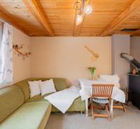 Innenraum einer Hütte mit Kachelofen, grünem Sofa und Tisch. Holzdecke und Dekorationen.