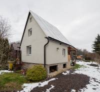 Ein Haus in Handlová mit Rasen und einem verschneiten Garten, umgeben von Bäumen und Sträuchern.