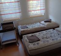 Ein Kinderbett und zwei Betten im Schlafzimmer mit einem Boden in Holzoptik.