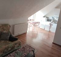 Dachboden in einem Einfamilienhaus mit Küche, einem Blumenmuster-Sofa und einem Boden in Holzoptik.