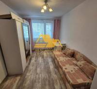 Ein Zimmer in einer 3-Zimmer-Wohnung mit einem Sofa, einem Schrank und einem Boden mit Holzdekor.