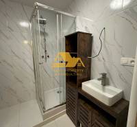 Badezimmer in einer 2-Zimmer-Wohnung mit weißen Fliesen, einer Duschkabine und einem Waschbecken auf einem Schrank.