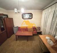 Ein Zimmer in einem Einfamilienhaus mit Möbeln, Vorhängen und einem Boden in Holzoptik.