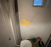 Badezimmer im Einfamilienhaus mit Toilette und kleinem Fenster, Eimer und Gießkanne.