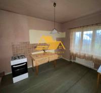 Eine Küche in einem Einfamilienhaus mit einem Herd, einem Tisch, einer Gardine und einer hellen Wanddekoration.