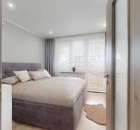 Schlafzimmer in einer 3-Zimmer-Wohnung mit Bett, Vorhängen und Boden mit Holzdekor.