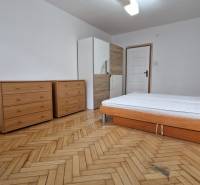 Schlafzimmer in einer 2-Zimmer-Wohnung mit Holzdekor auf dem Boden, Bett und Kommoden.