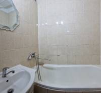 Ein Badezimmer in einer 2-Zimmer-Wohnung mit Badewanne, Waschbecken und Spiegel, gefliest mit beigen Fliesen.