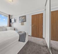 Helles Schlafzimmer mit Bett, großem Fenster und Kleiderschrank in einer 2-Zimmer-Wohnung.