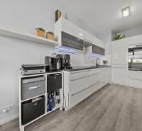 Küche in einer 2-Zimmer-Wohnung mit weißen Schränken und einem Boden in Holzoptik.