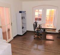 Ein Büro mit einem Fenster, einem Regal, zwei Stühlen und einem Boden mit Holzdekor.