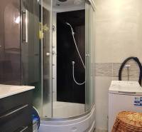 Badezimmer in einer 2-Zimmer-Wohnung mit Duschkabine und Waschmaschine, Fliesen mit Holzdekor.